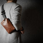 Person wearing a brown leather crossbody bag against a dark background