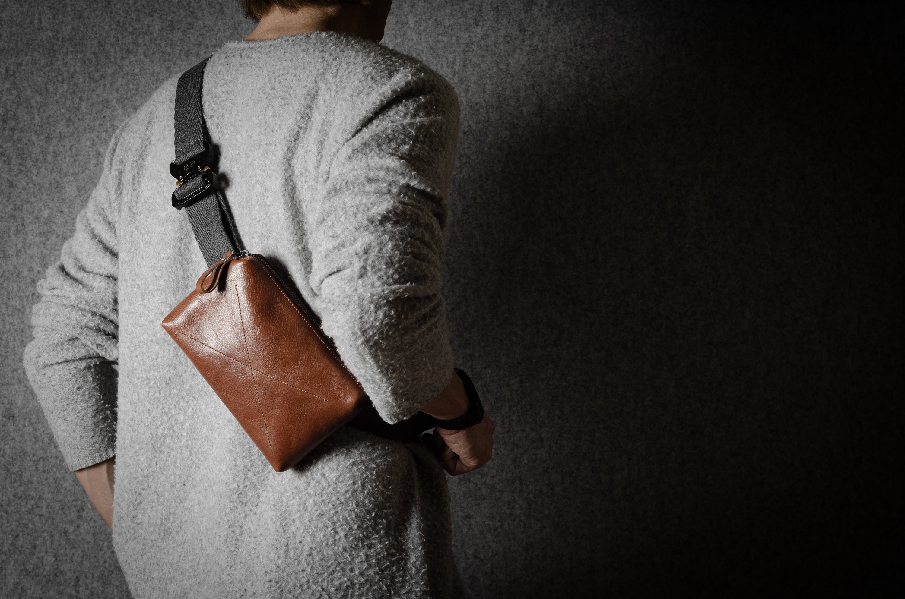 Person wearing a brown leather crossbody bag against a dark background
