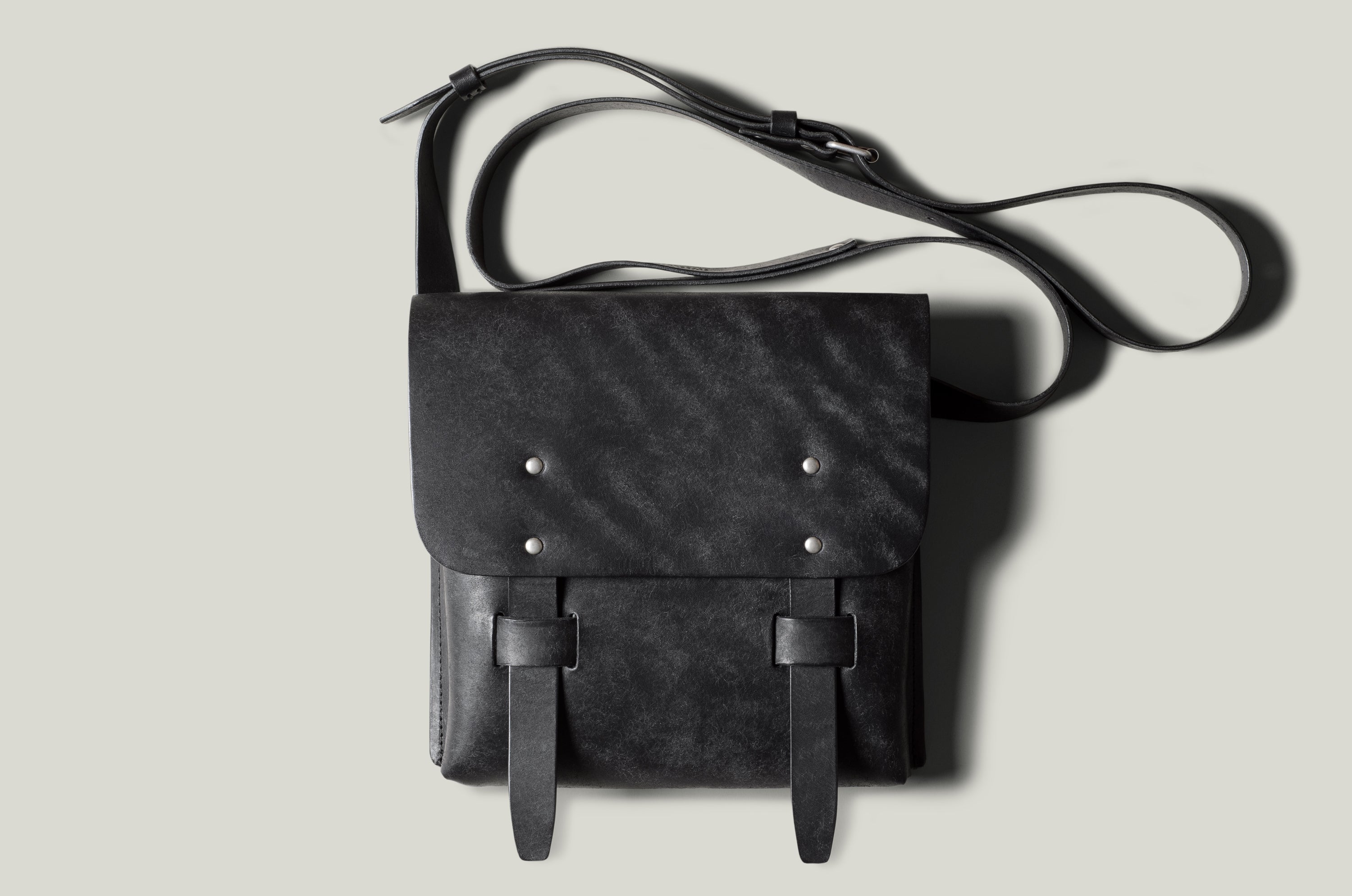 Black leather bag with strap on a light gray background