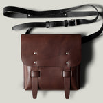 Brown leather bag with a black strap on a light gray background