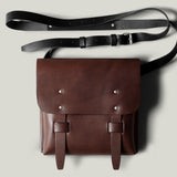 Brown leather bag with a black strap on a light gray background