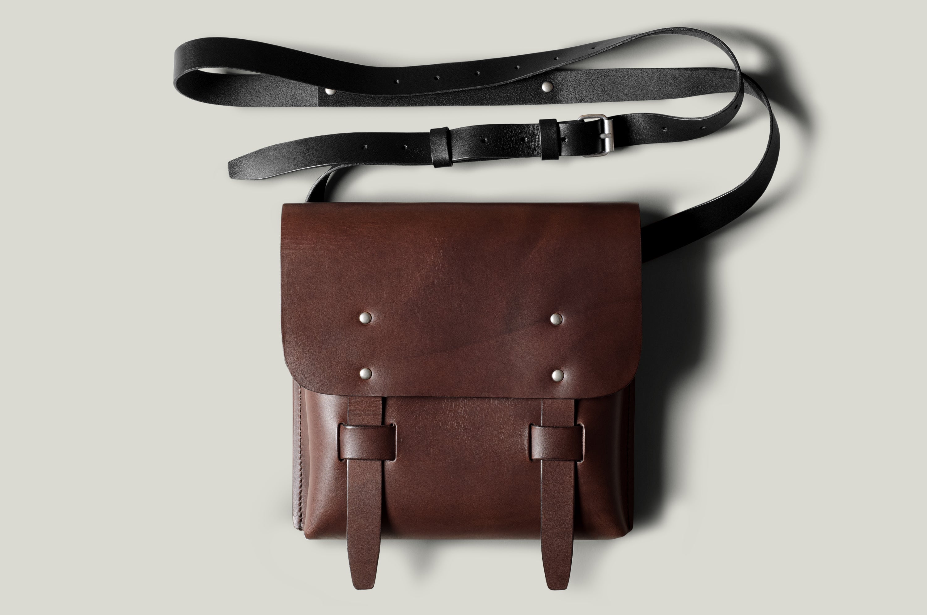 Brown leather bag with a black strap on a light gray background