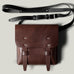 Brown leather bag with a black strap on a light gray background