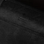 Close-up of a black leather bag with visible stitching and brand name on a dark background
