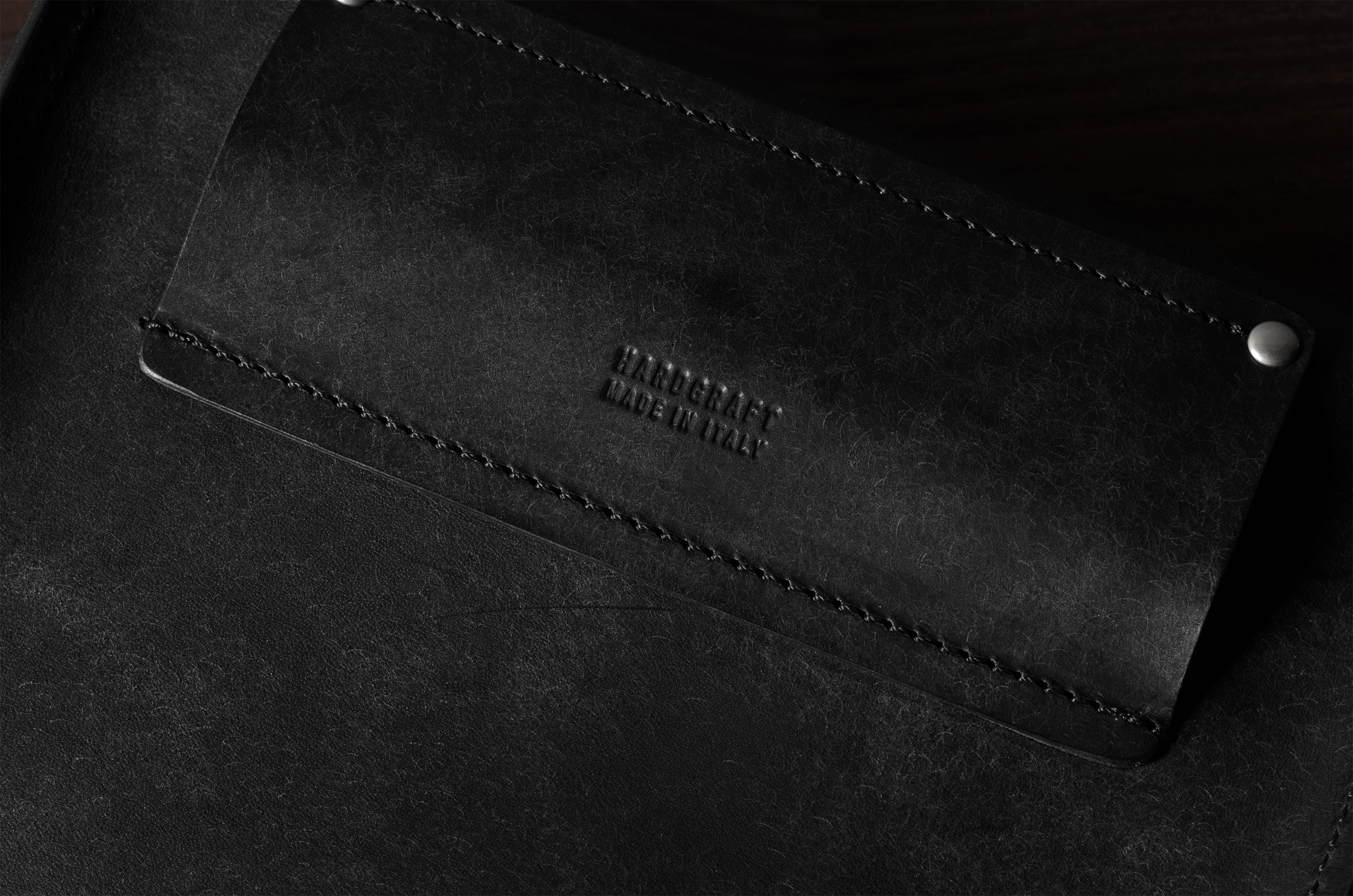 Close-up of a black leather bag with visible stitching and brand name on a dark background