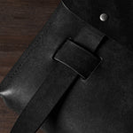 Close-up of a black bag with a belt and metal rivet on a wooden surface