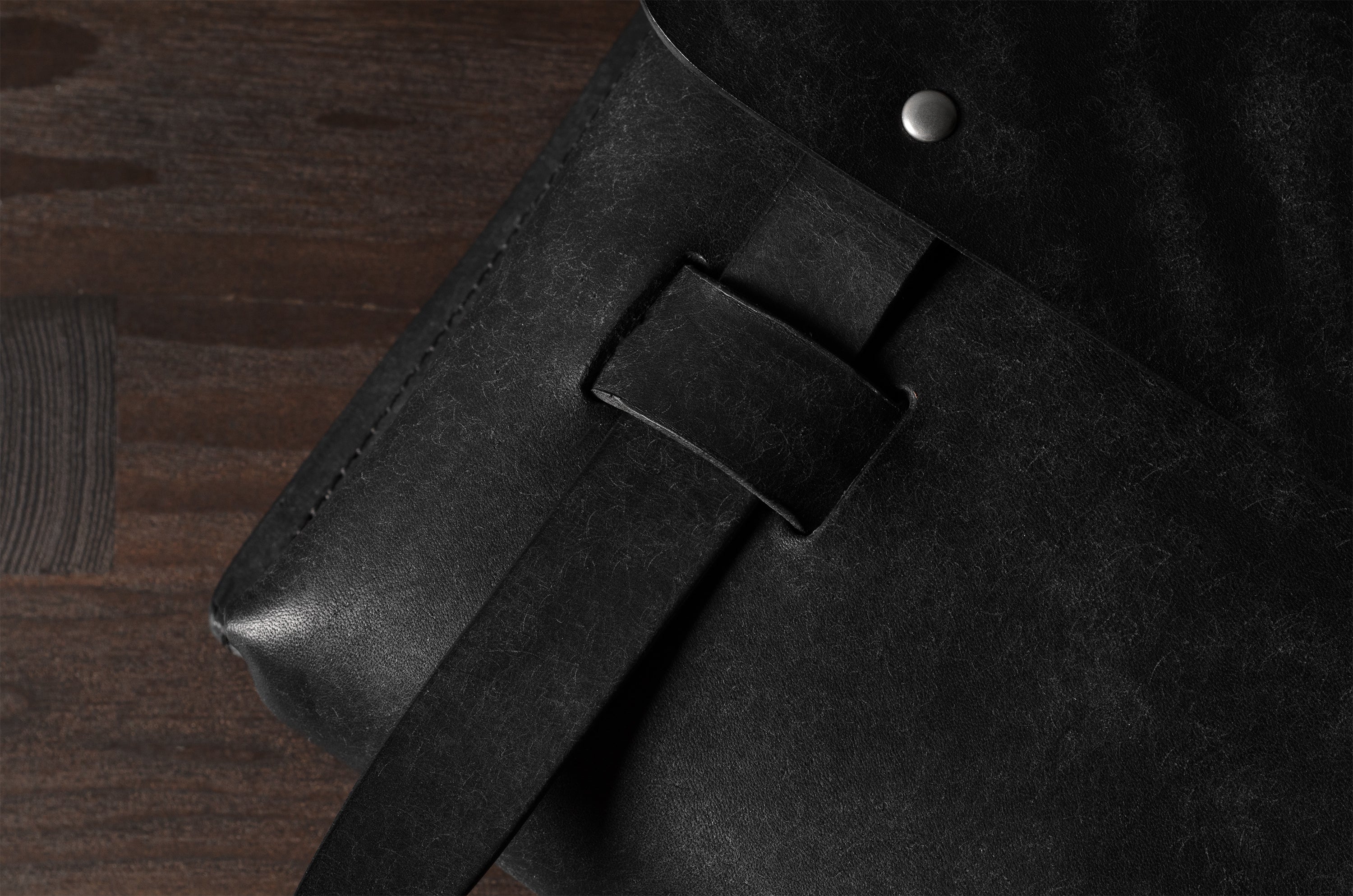 Close-up of a black bag with a belt and metal rivet on a wooden surface