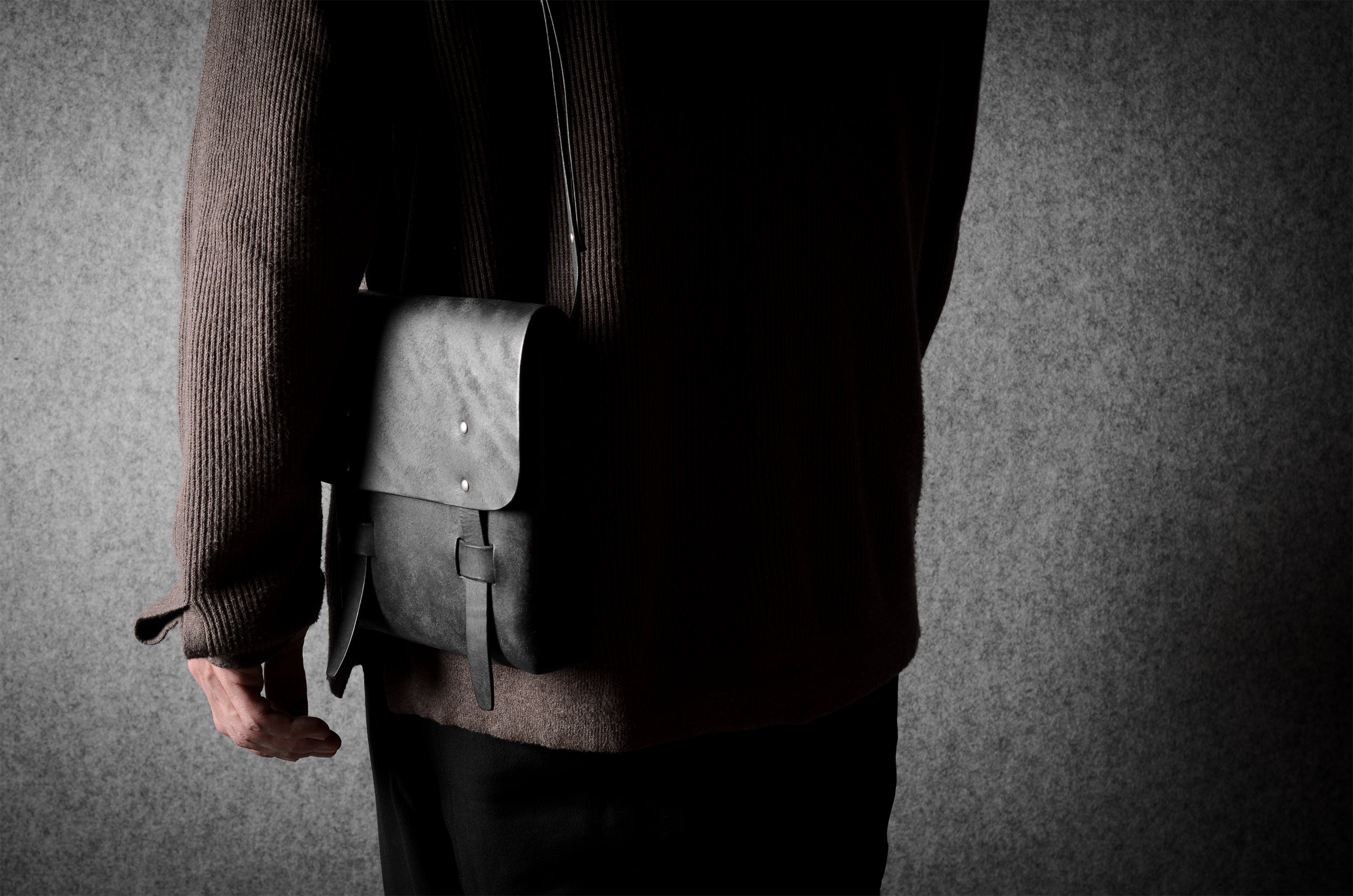 Person holding a black  leather bag against a gray background