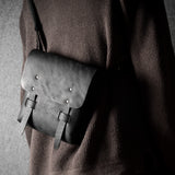 Person wearing a dark sweater with a gray leather satchel bag on a plain background