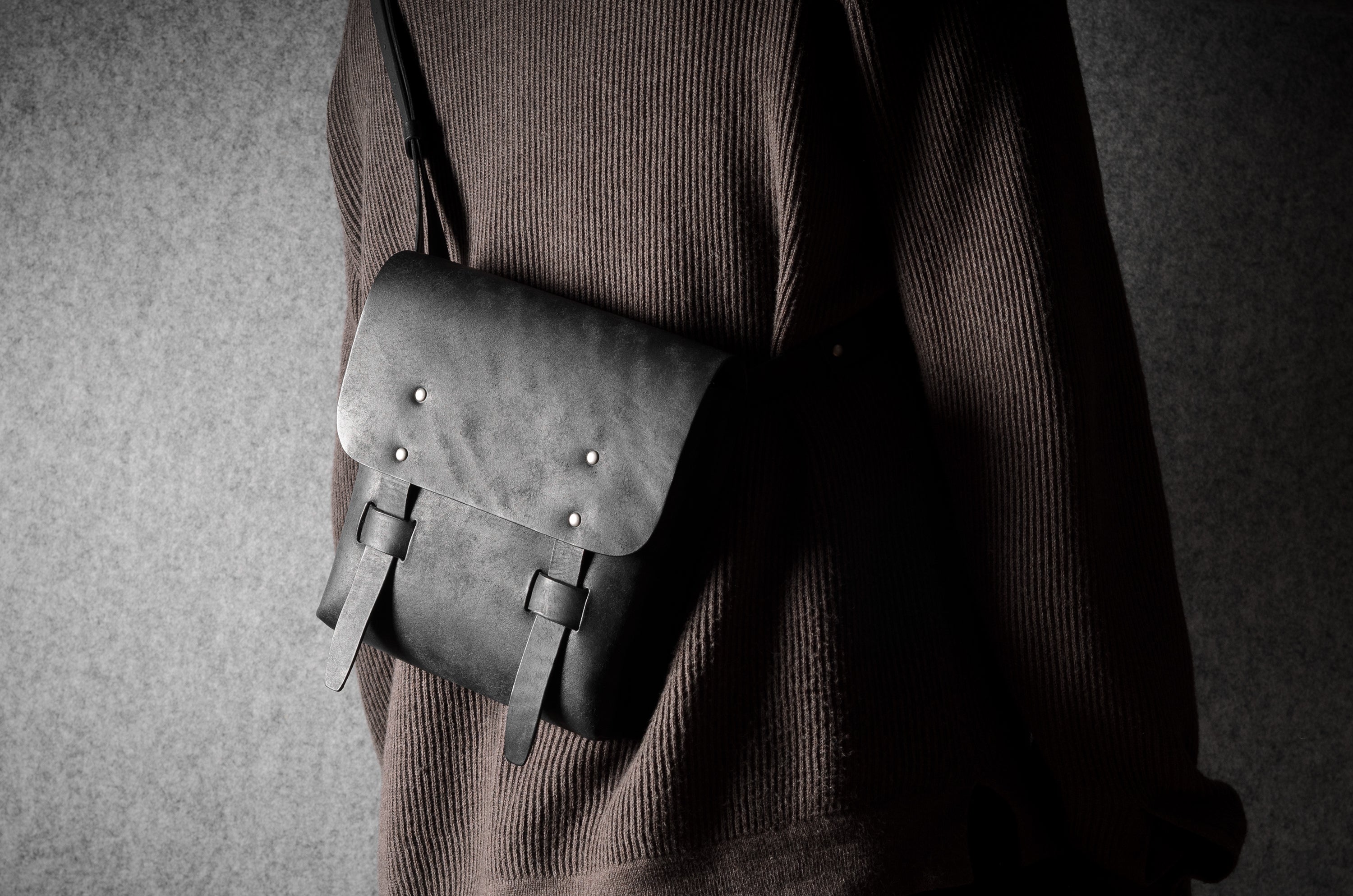 Person wearing a dark sweater with a gray leather satchel bag on a plain background