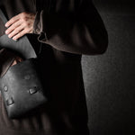 Person holding a black leather bag against a dark background
