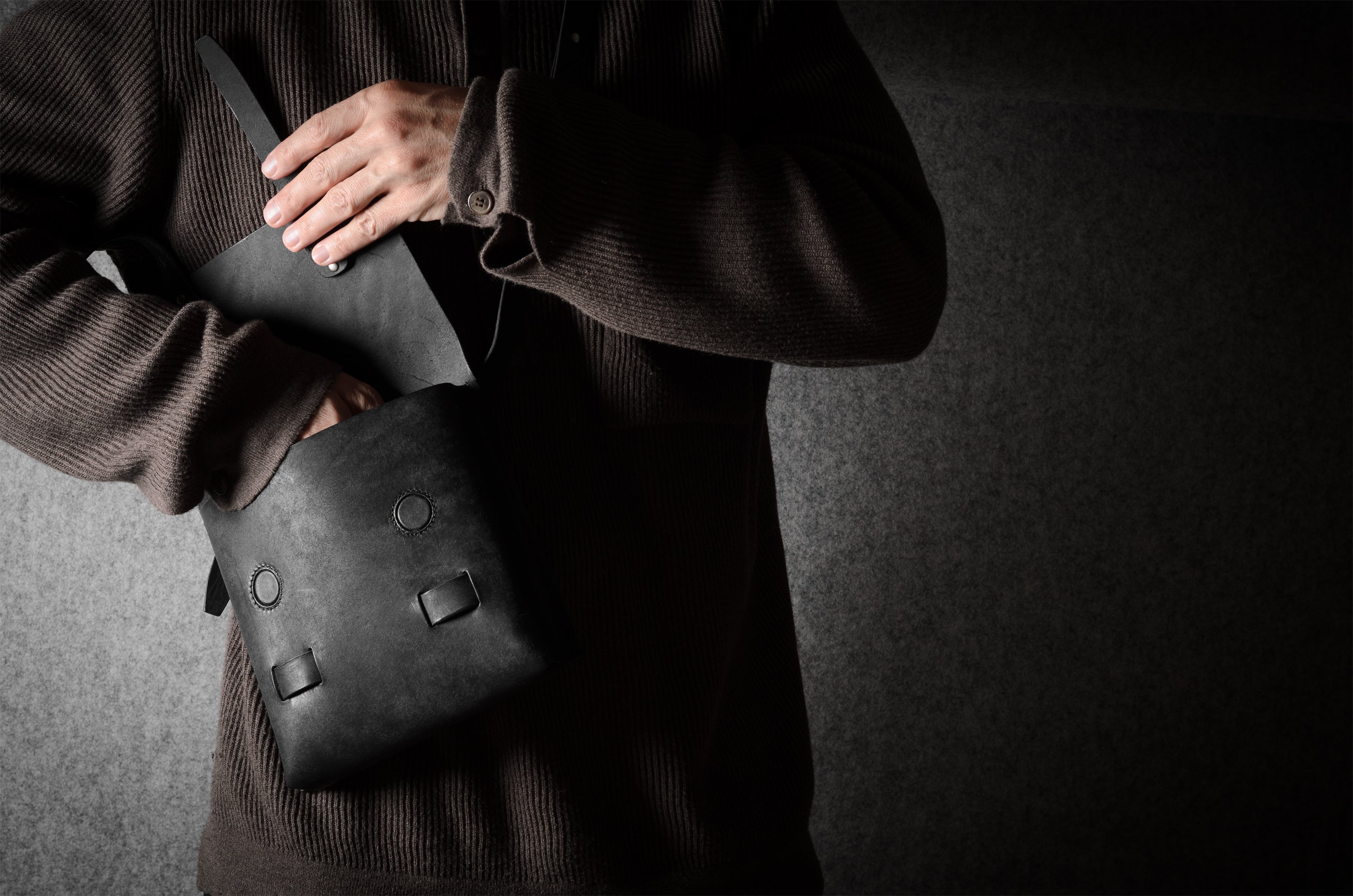 Person holding a black leather bag against a dark background