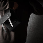 Person wearing a dark sweater with a black bag on a gray background