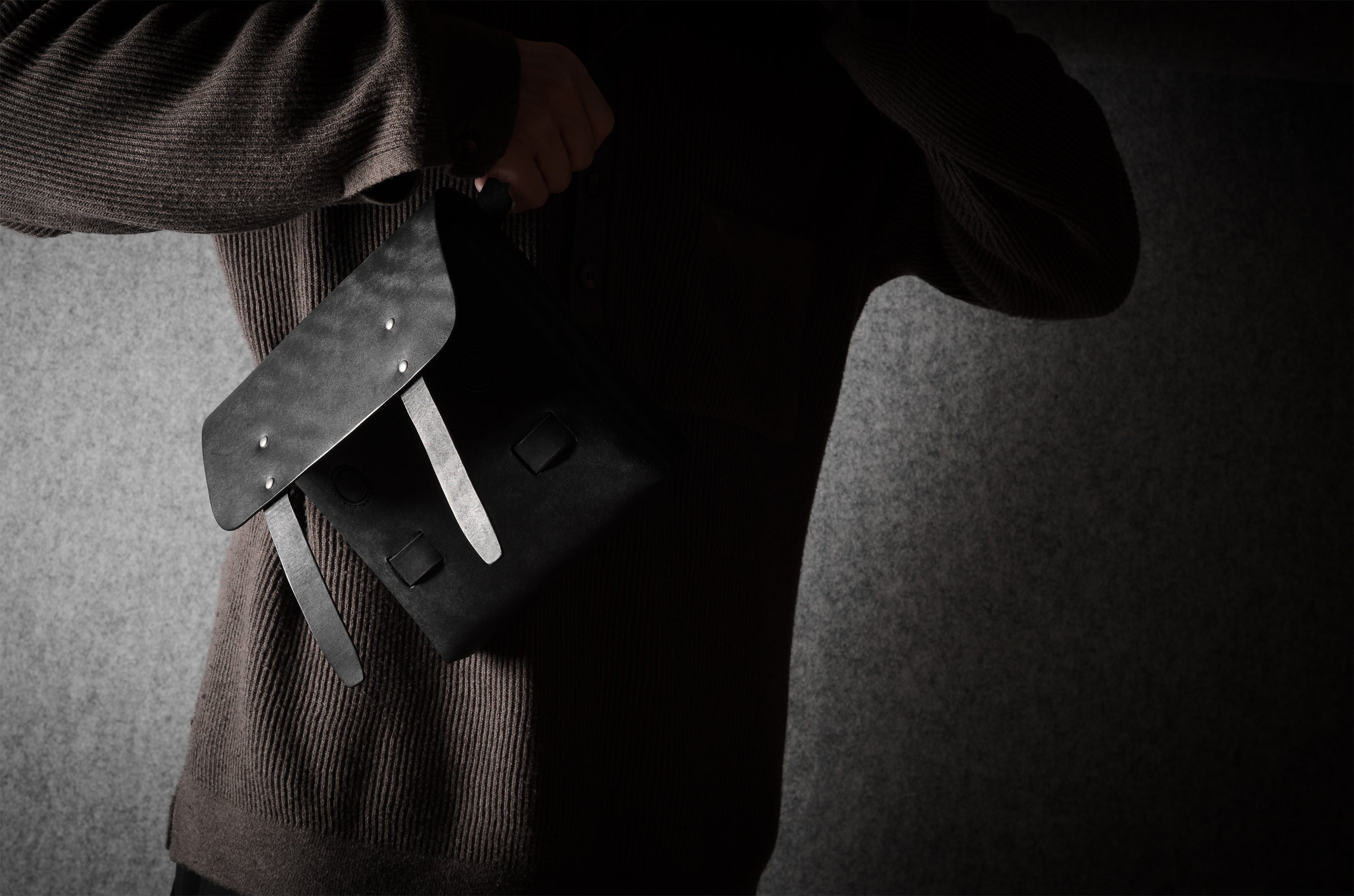 Person wearing a dark sweater with a black bag on a gray background