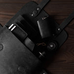 Black leather bag with multiple small leather goods on a wooden surface
