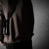 Person wearing a brown sweater with a black bag with a dark background
