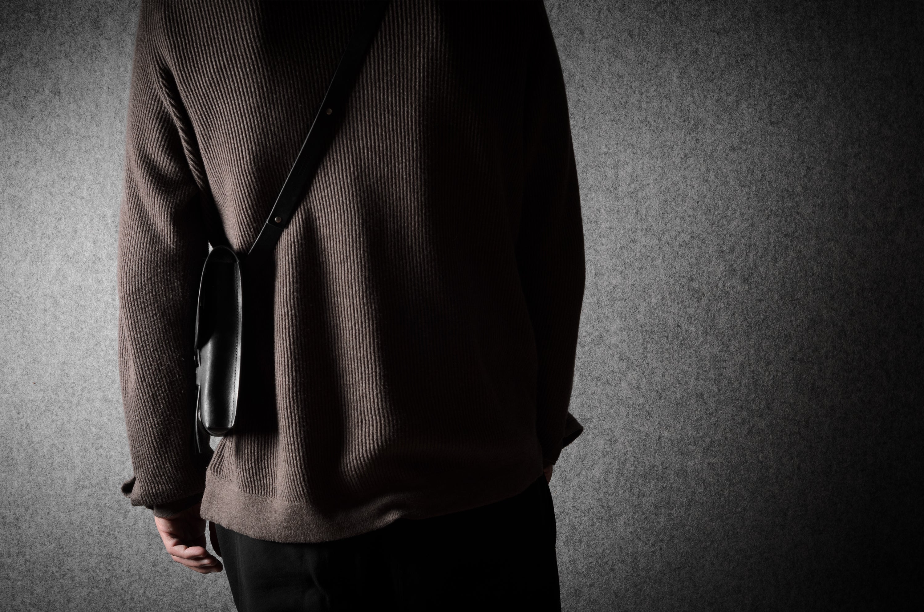 Person wearing a brown sweater with a black bag with a dark background