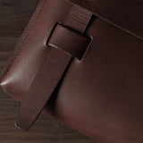 Close-up of a brown leather bag with a leather strap on a wooden surface