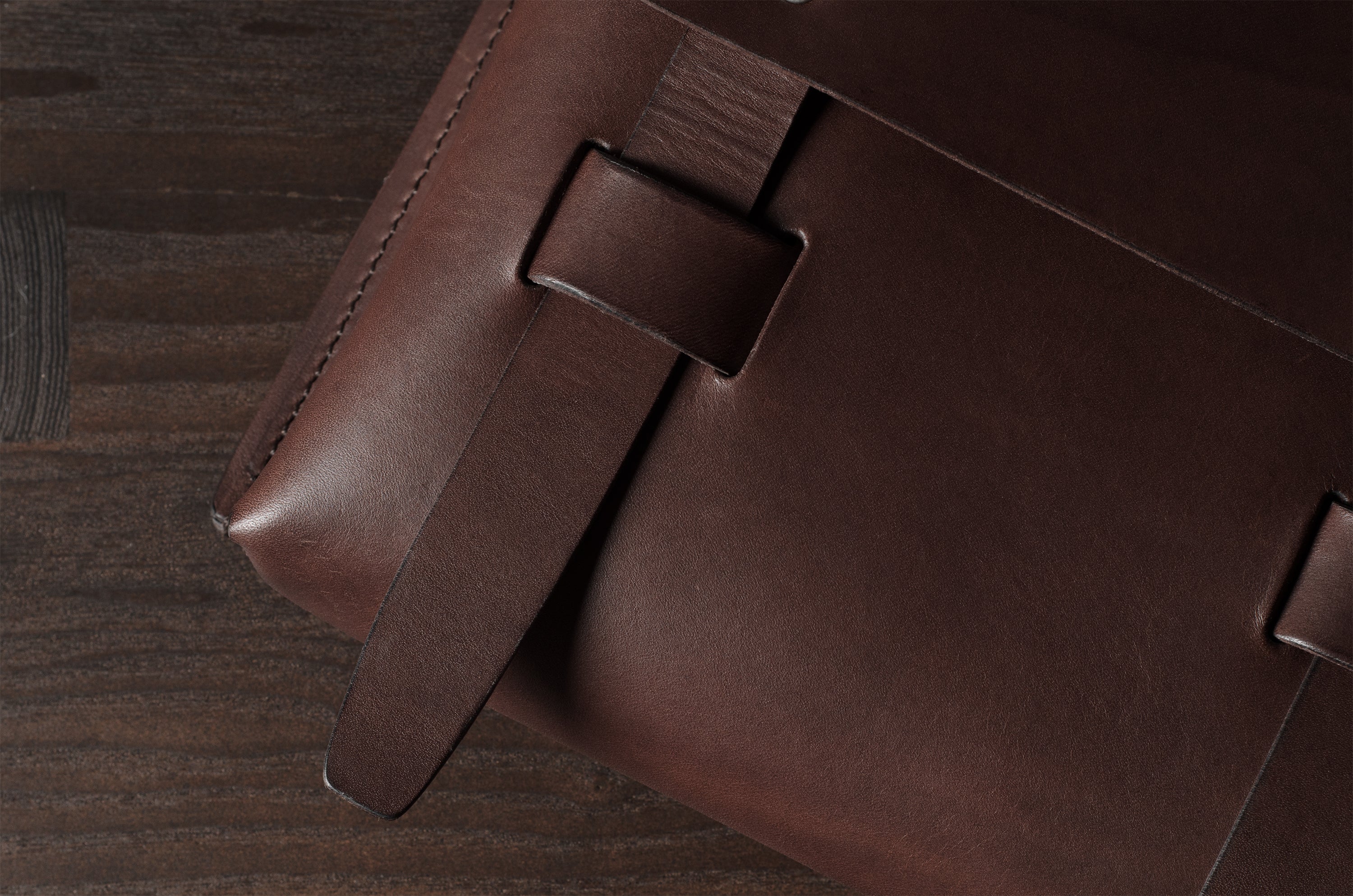 Close-up of a brown leather bag with a leather strap on a wooden surface