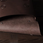 Close-up of a brown leather bag with rivets on a wooden surface