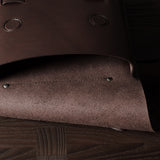 Close-up of a brown leather bag with rivets on a wooden surface