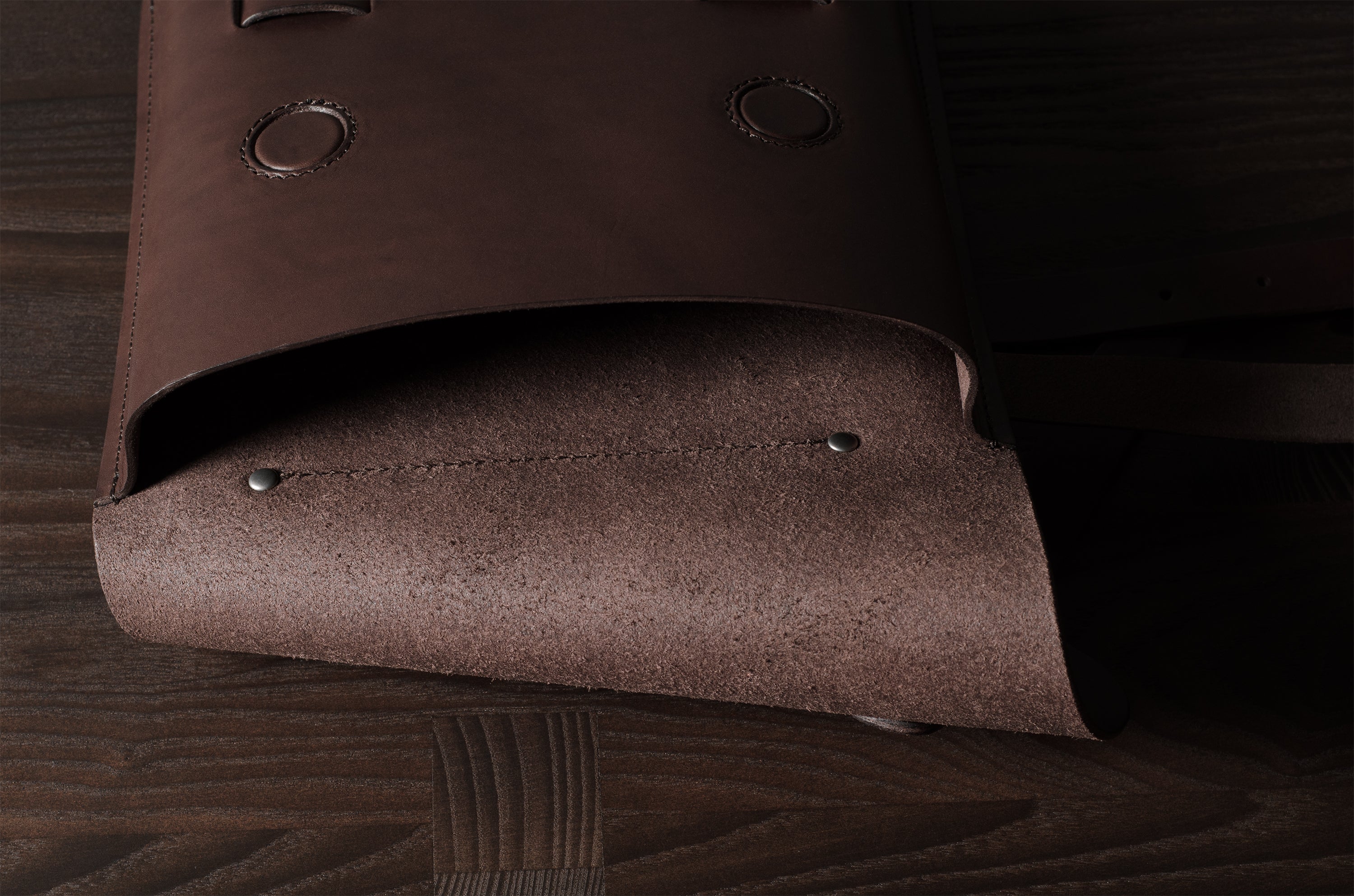 Close-up of a brown leather bag with rivets on a wooden surface