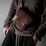 Person wearing a brown sweater with a brown leather satchel over one shoulder against a gray background