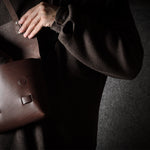 Person holding a brown leather bag against a dark background