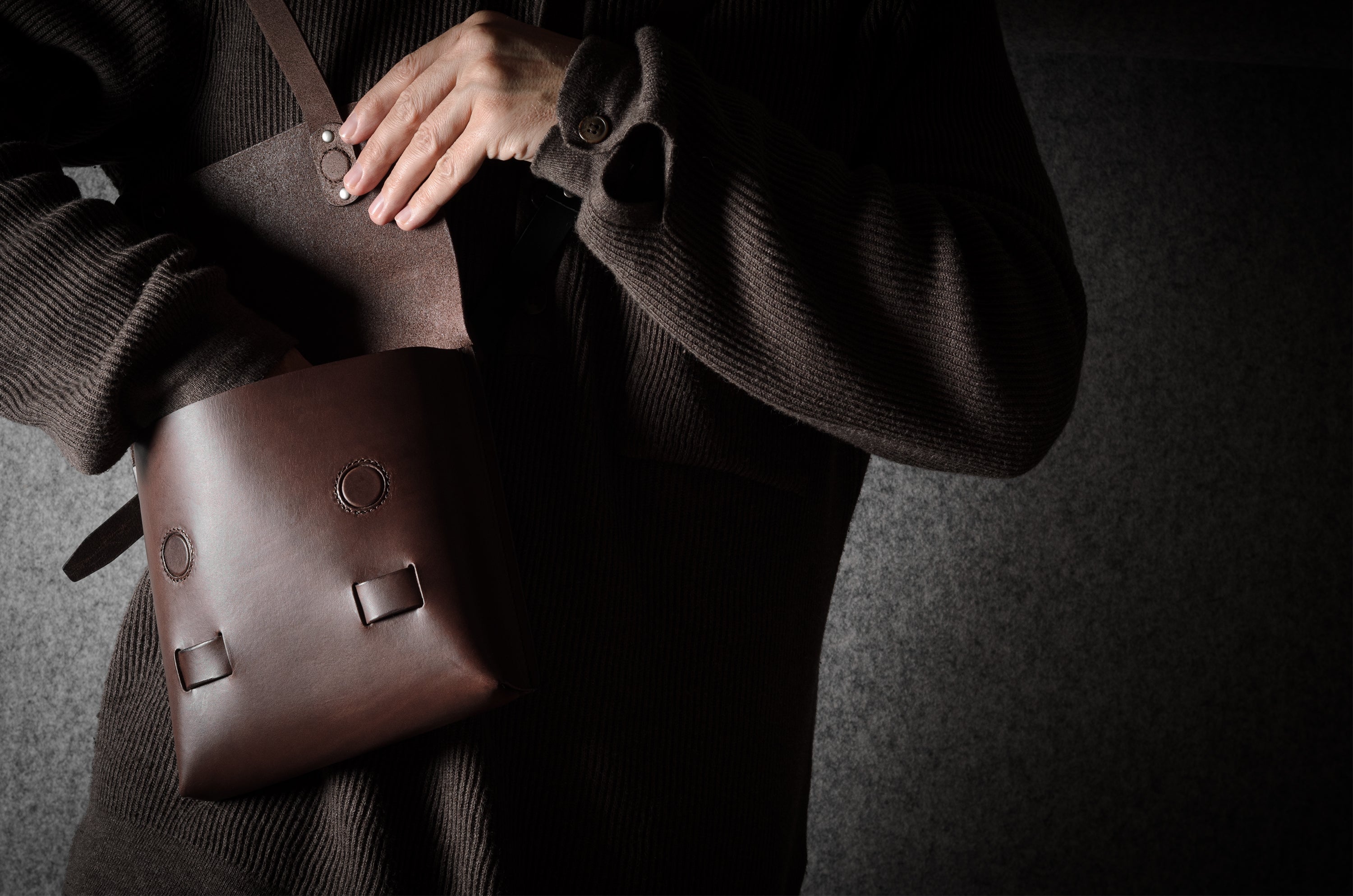 Person holding a brown leather bag against a dark background