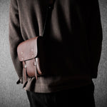 Person holding a brown leather satchel against a gray background