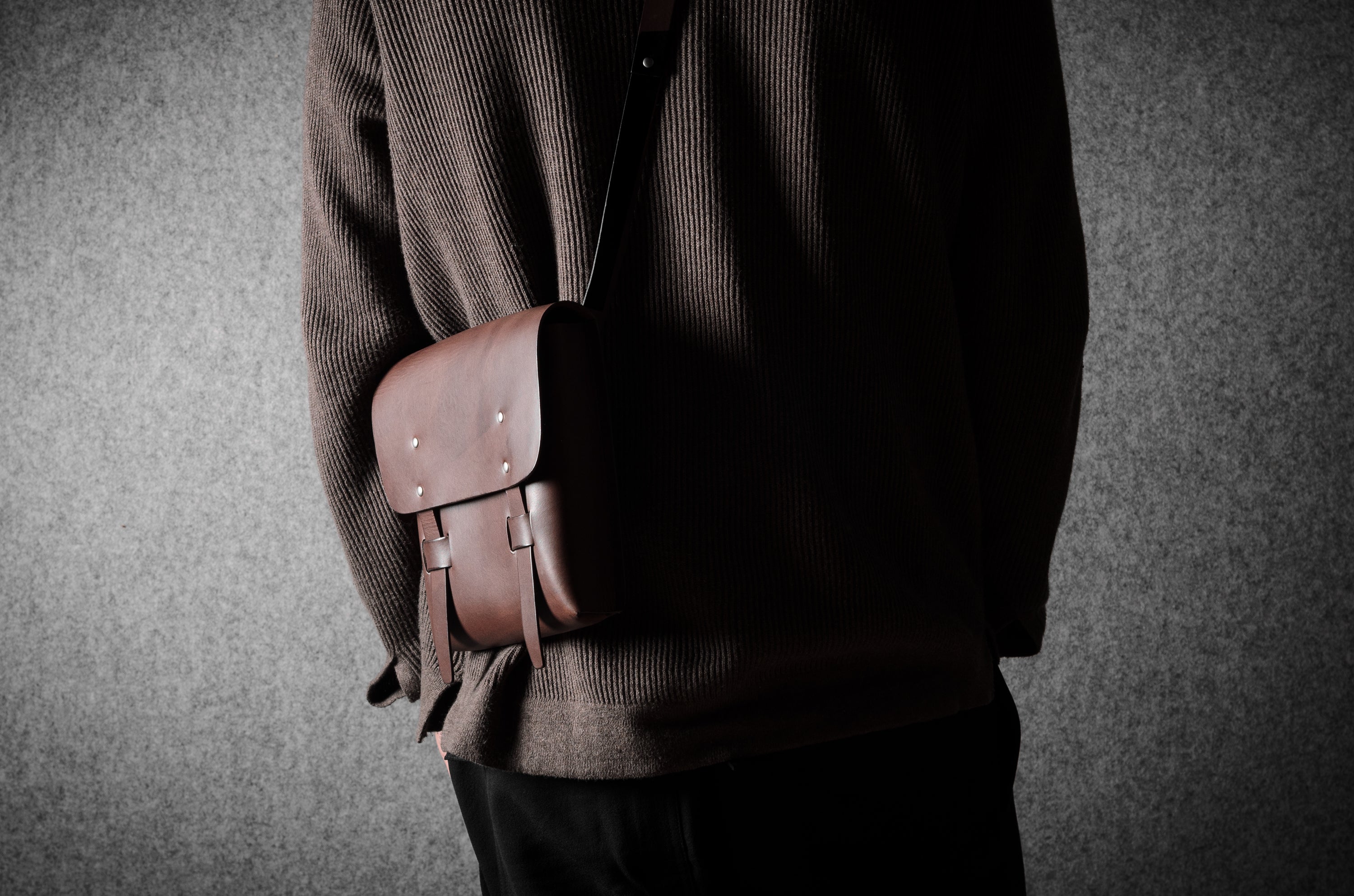 Person holding a brown leather satchel against a gray background