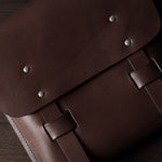Brown leather satchel with metal rivets on a wooden surface