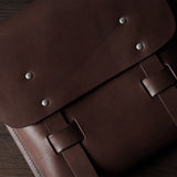 Brown leather satchel with metal rivets on a wooden surface