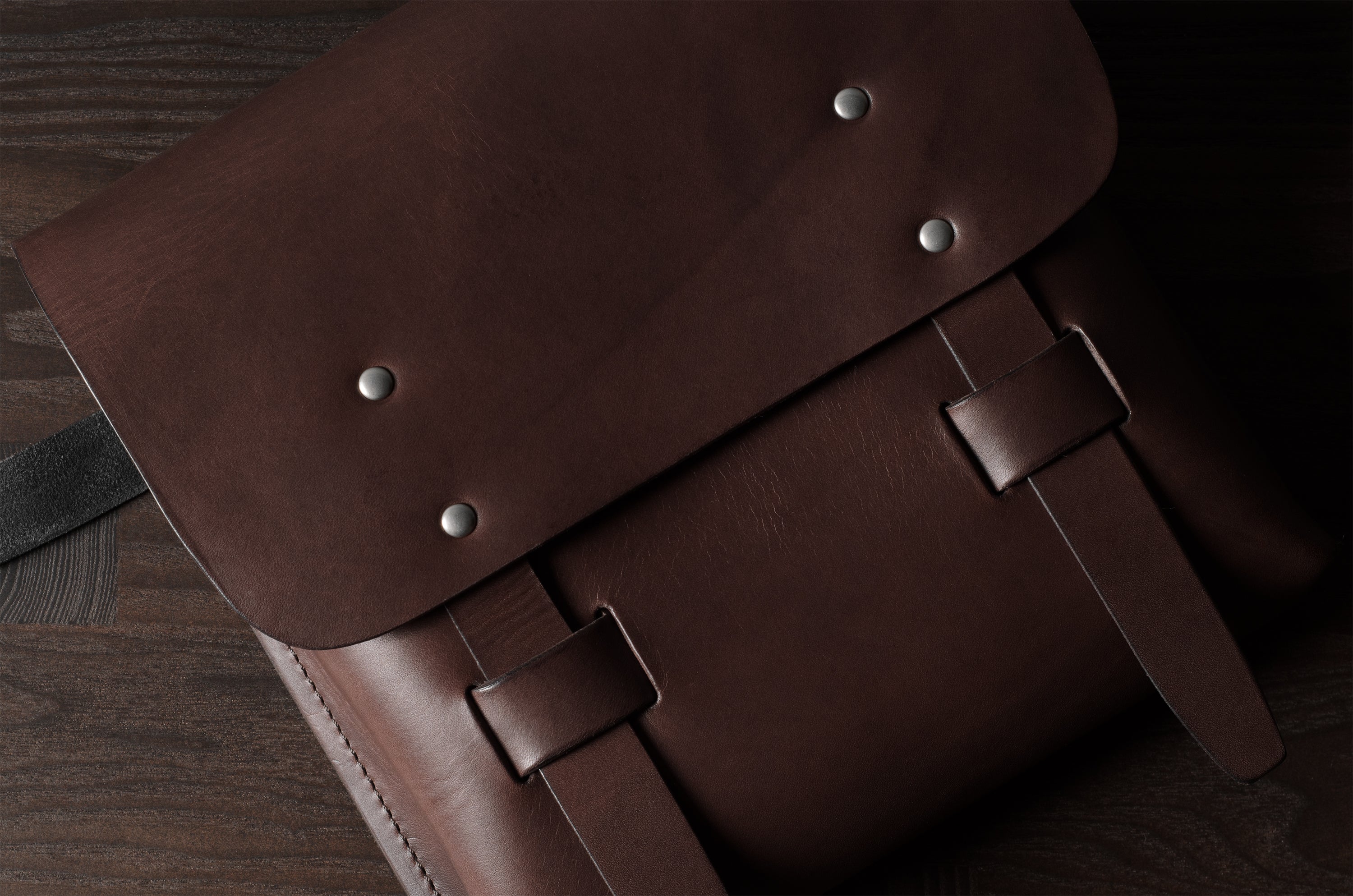 Brown leather satchel with metal rivets on a wooden surface
