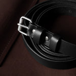 Black leather belt with silver buckle on a brown leather surface