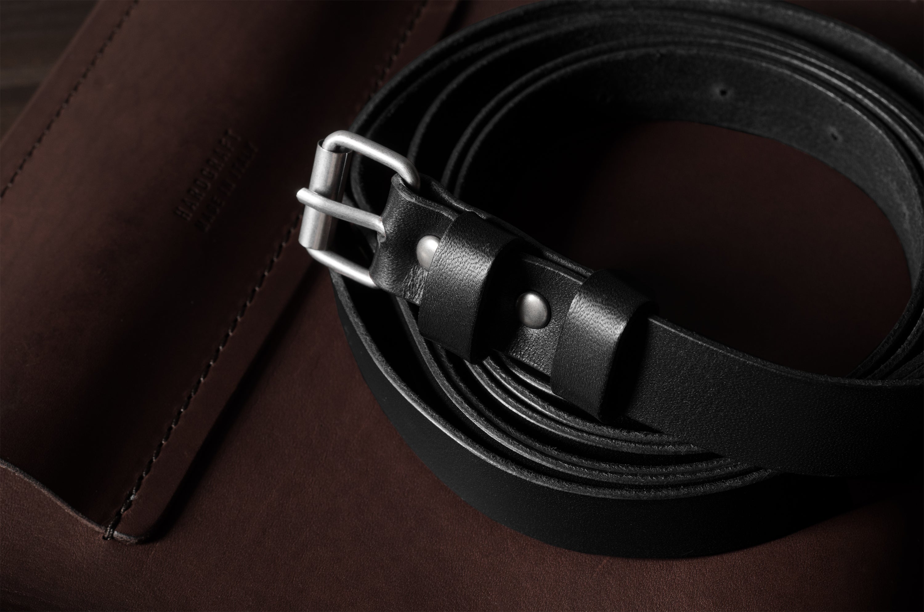 Black leather belt with silver buckle on a brown leather surface