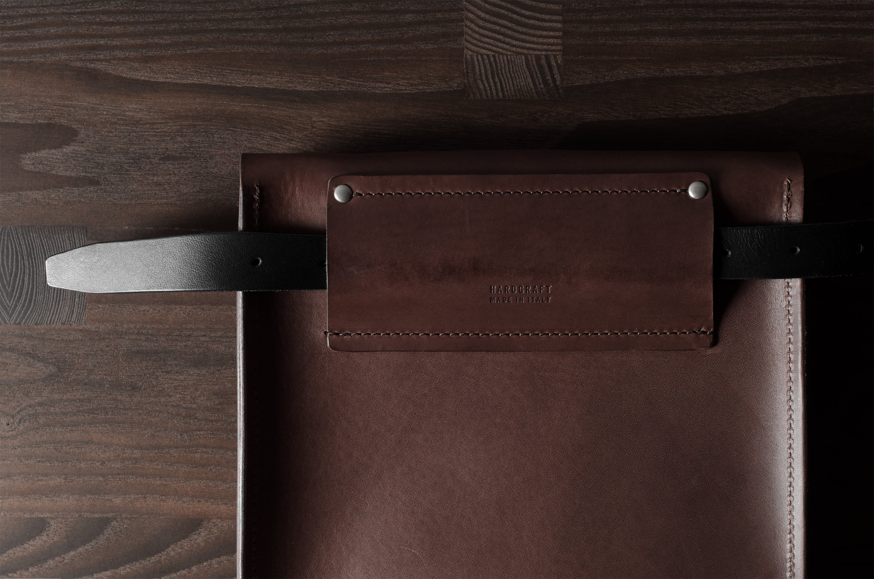 Brown leather bag with a strap on a wooden surface