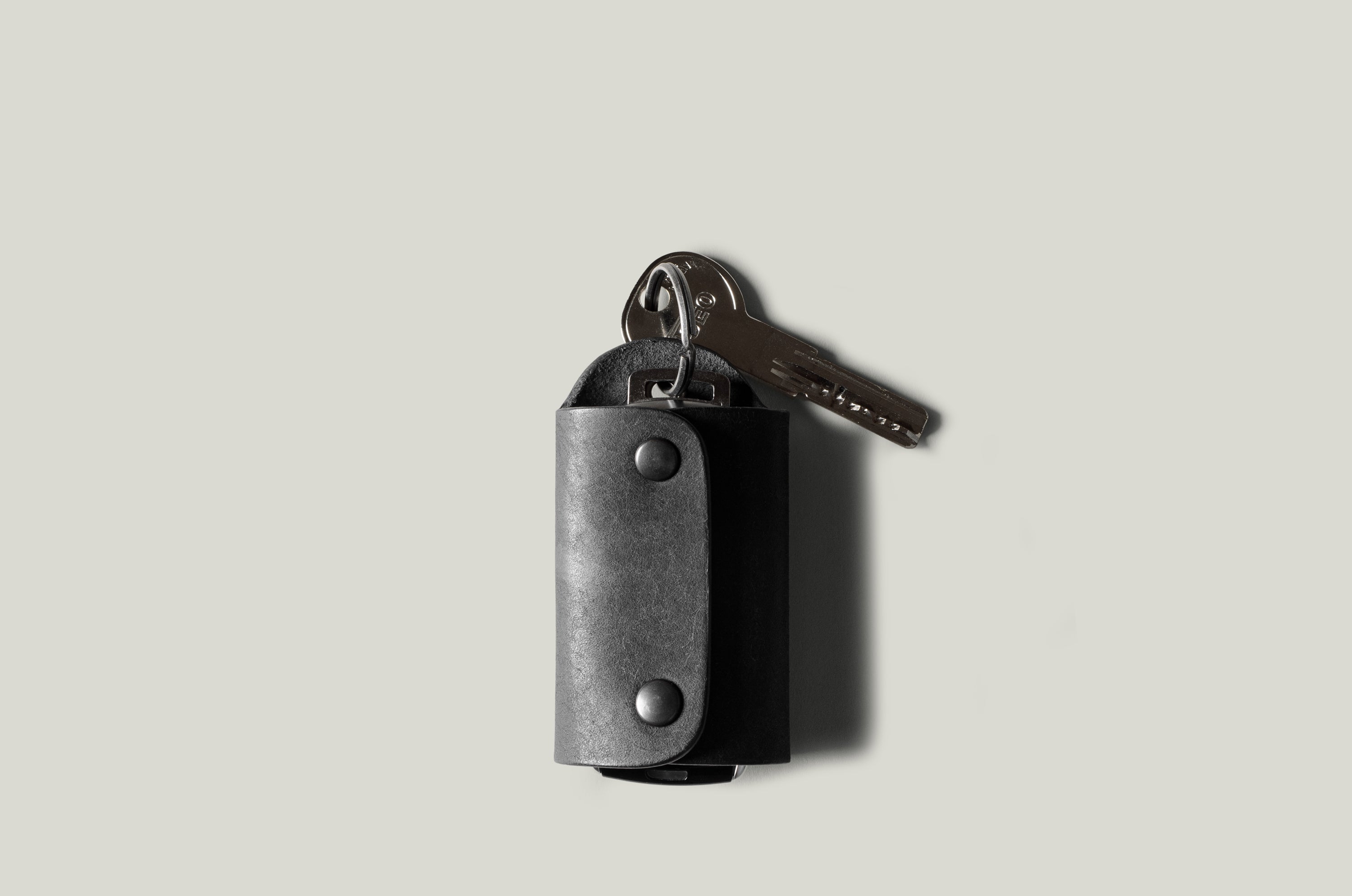 Black leather key holder with 2 metal buttons on light grey background