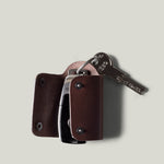 Dark brown leather key holder with 2 metal buttons, showing car key fob and key on light grey background