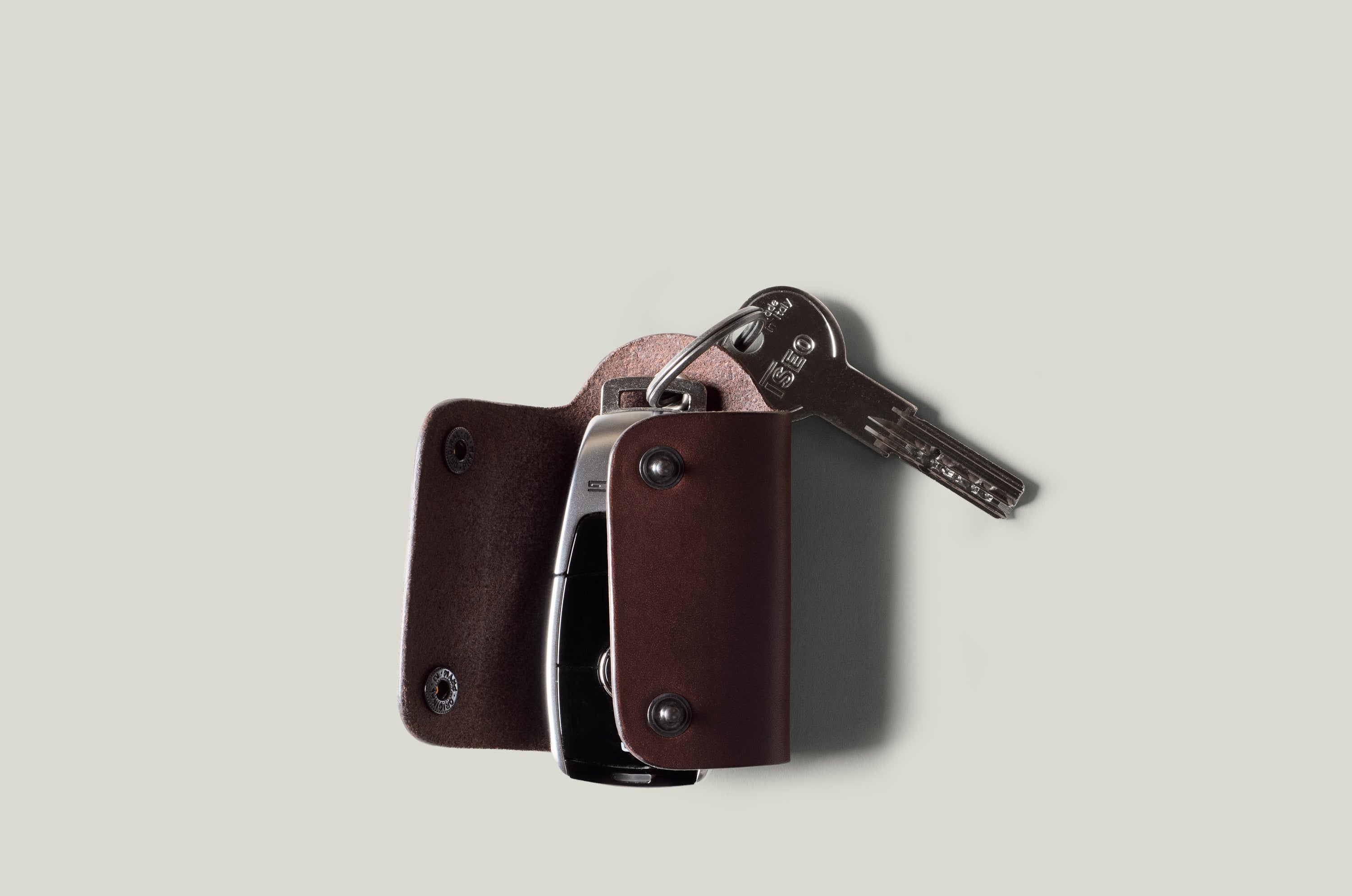 Dark brown leather key holder with 2 metal buttons, showing car key fob and key on light grey background