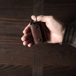 Dark brown leather key holder with keyring, held in hand on wood background