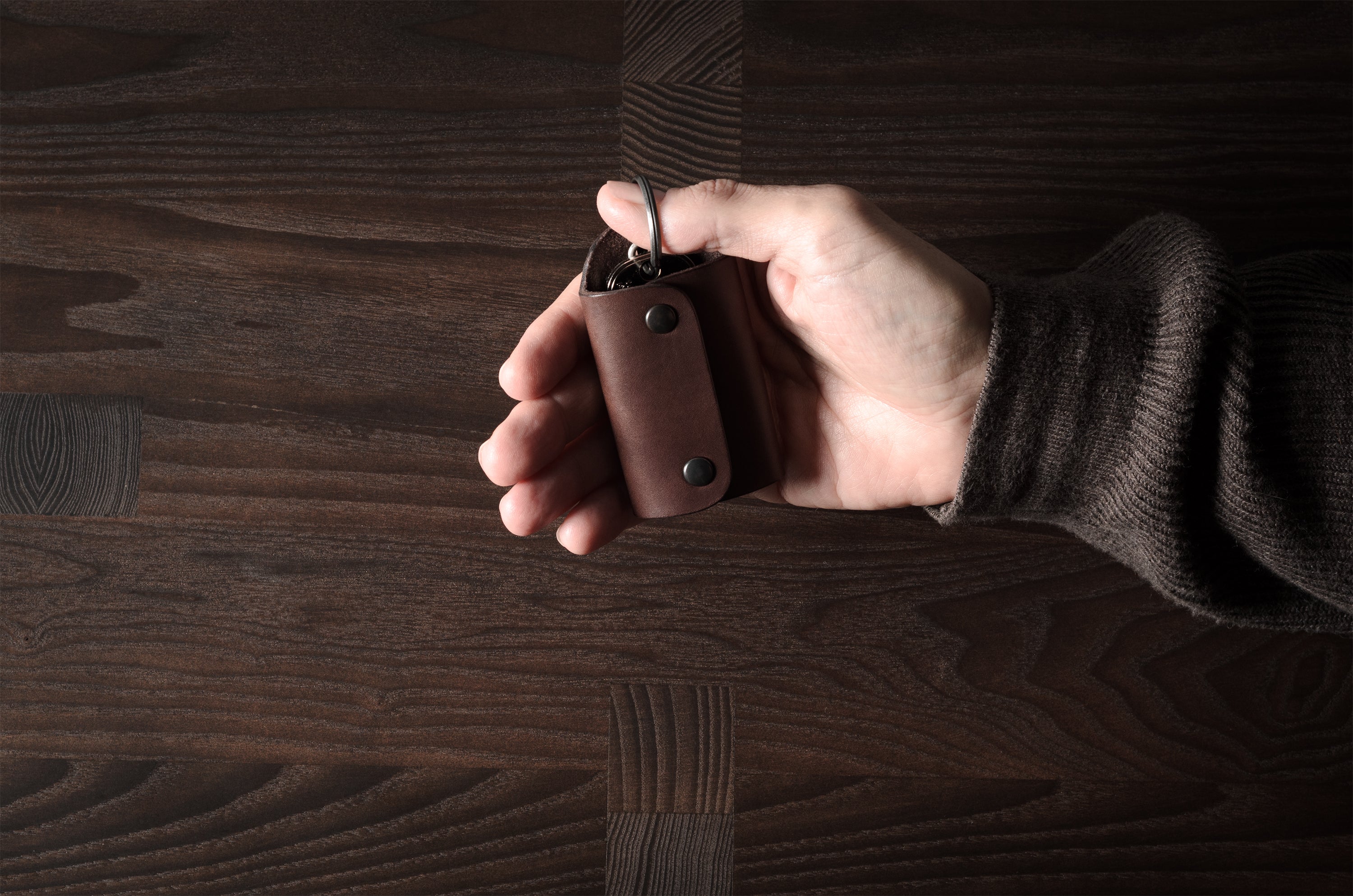 Dark brown leather key holder with keyring, held in hand on wood background