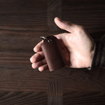 Dark brown leather key holder with keyring, held in hand on wood background
