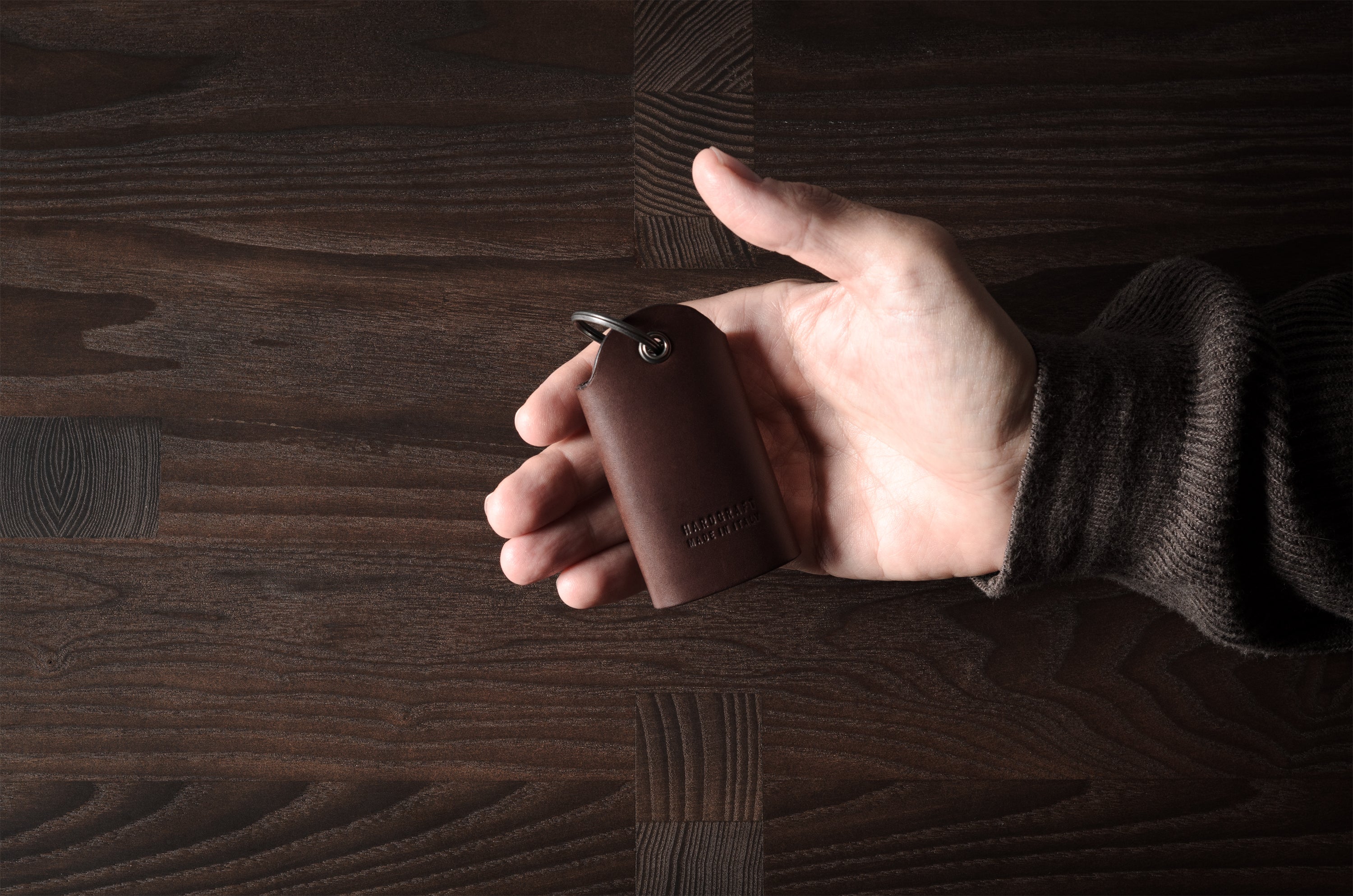 Dark brown leather key holder with keyring, held in hand on wood background
