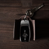 Dark brown leather key holder with keyring, key and car key fob on wood background