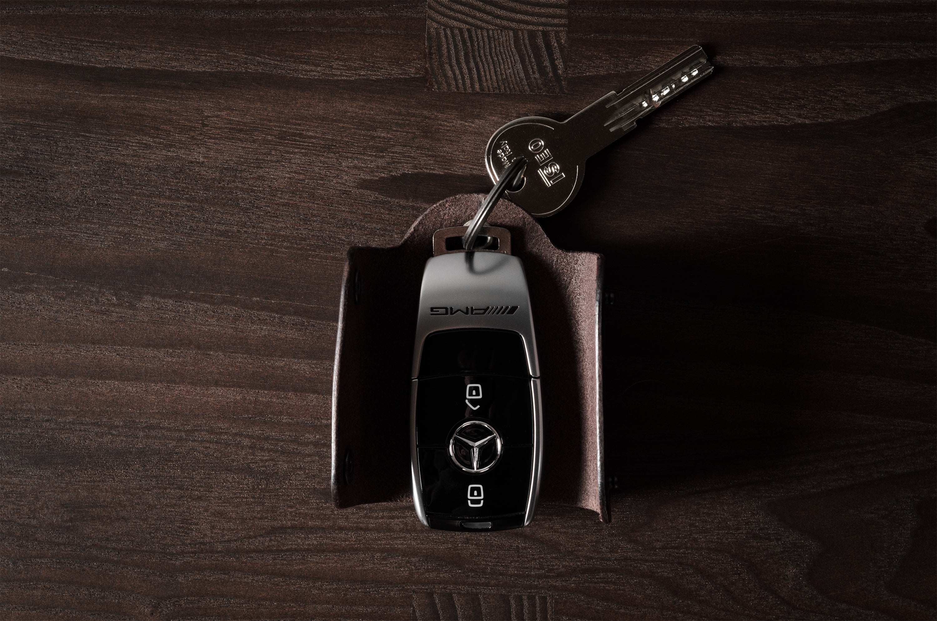 Dark brown leather key holder with keyring, key and car key fob on wood background