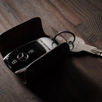 Dark brown leather key holder with keyring, key and car key fob on wood background