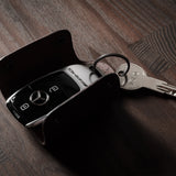 Dark brown leather key holder with keyring, key and car key fob on wood background