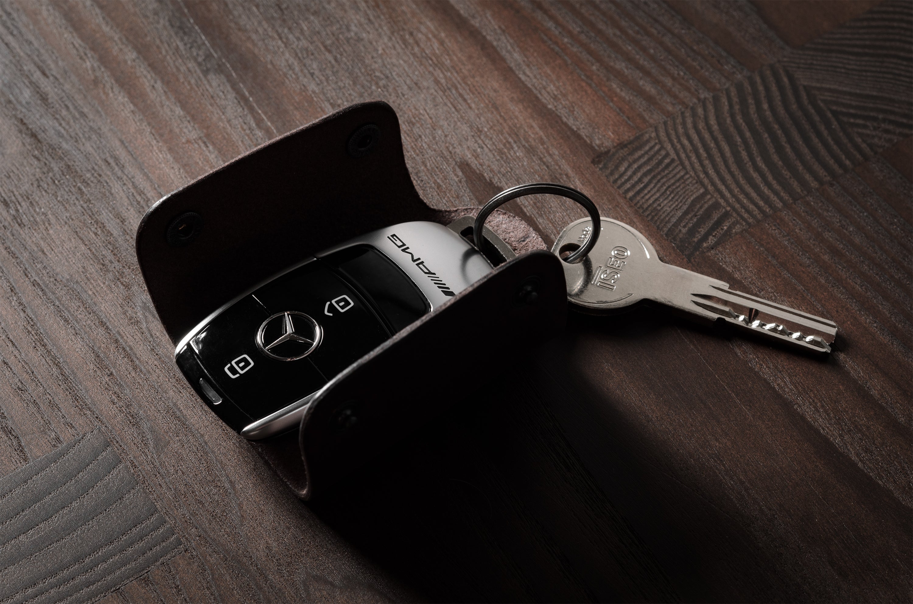 Dark brown leather key holder with keyring, key and car key fob on wood background