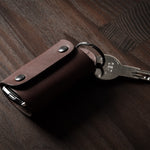 Dark brown leather key holder with keyring, key and car key fob on wood background